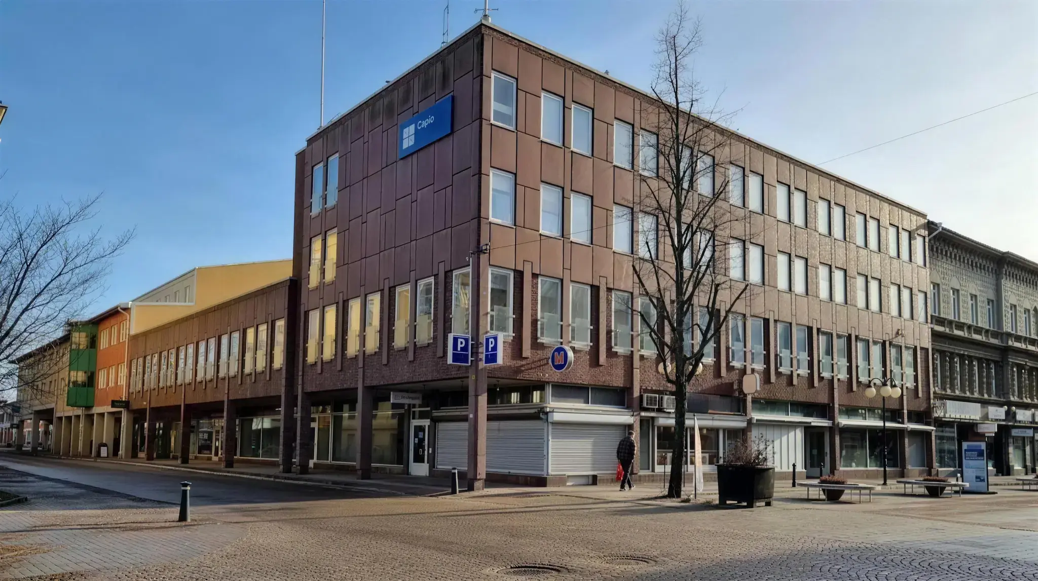 Bild på torg, brun byggnad förbipasserare och gå-gata